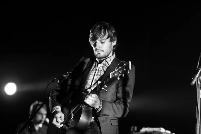 a man in a suit playing a guitar, a black and white photo, by Etienne Delessert, radiohead, tom burke, meadows, leonardo dicaprio