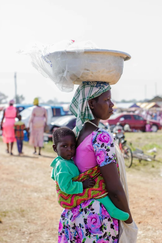 a woman carrying a child on her back, by Ingrida Kadaka, trending on unsplash, happening, market stalls, square, in 2 0 1 5, digital image