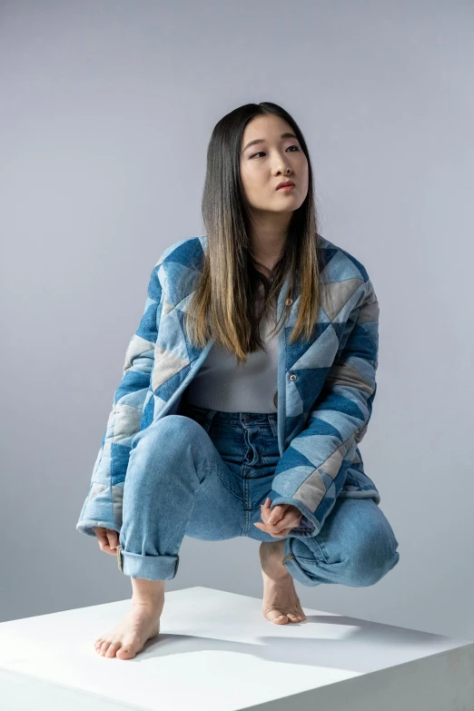 a woman sitting on top of a white box, an album cover, inspired by Kim Tschang Yeul, trending on unsplash, hyperrealism, model wears a puffer jacket, blue and grey, patterned clothing, wearing blue jean overalls