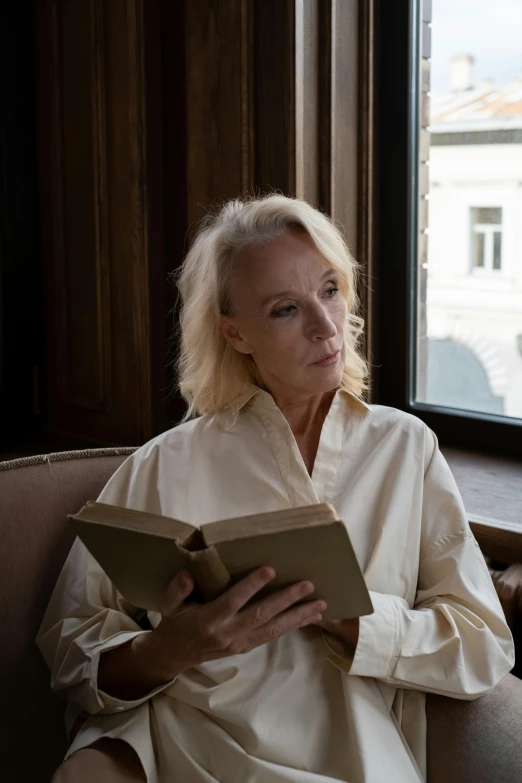 a woman sitting in a chair reading a book, a portrait, by Dietmar Damerau, trending on unsplash, albino, wearing a linen shirt, still from a movie, olga zakharova