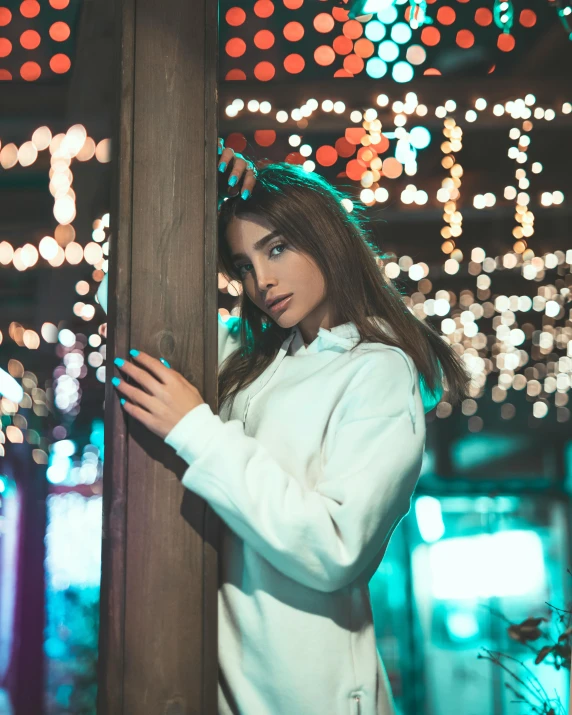 a woman leaning against a pole with christmas lights in the background, inspired by Elsa Bleda, trending on pexels, happening, wearing a white sweater, attractive androgynous humanoid, colorful picture, instagram picture