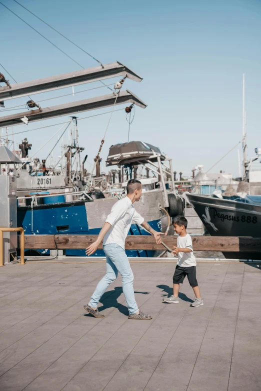 a man and a child walking in front of a boat, doing a kick, shipping docks, lachlan bailey, public space