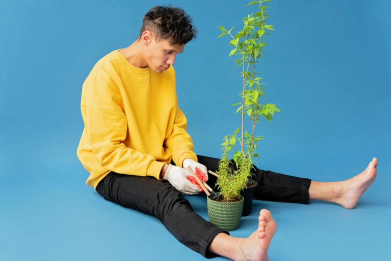 a man sitting on the ground holding a potted plant, inspired by David Hockney, pexels contest winner, antipodeans, pete davidson, press shot, multicoloured, joints