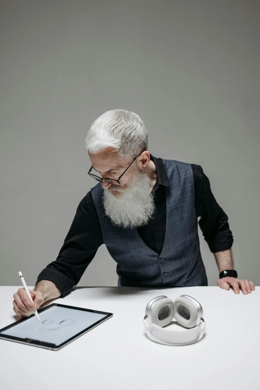 a man sitting at a table writing on a tablet, inspired by John Byrne, very long silver beard, wearing vr goggles, nadav kander, on grey background