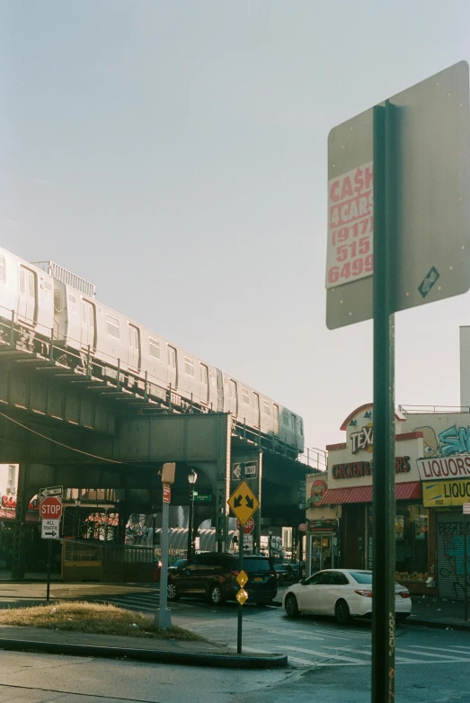 a train traveling over a bridge over a street, inspired by Elsa Bleda, petra collins, lots of signs, 1990s photograph, street corner