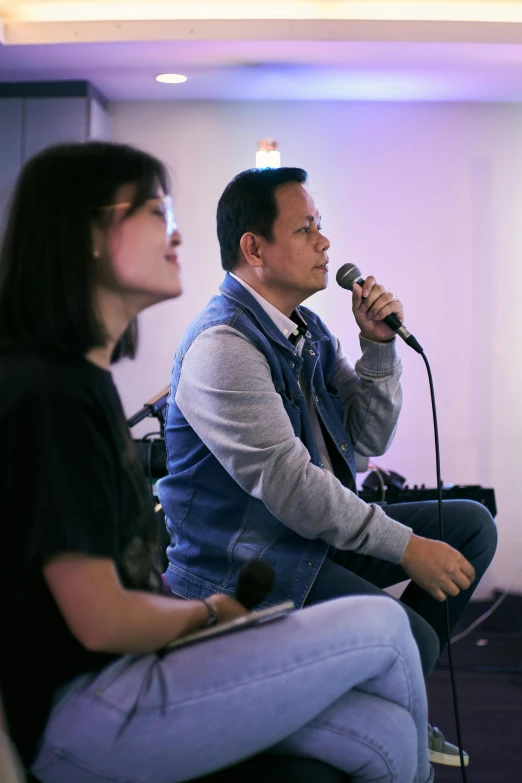 a man and a woman sitting next to each other, an album cover, by Robbie Trevino, pexels, giving a speech, asian man, worship, in a workshop