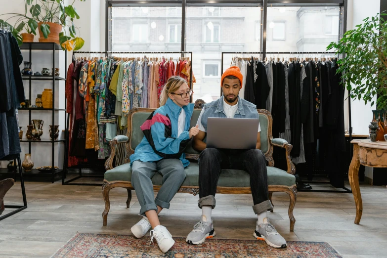 a man and woman sitting on a couch looking at a laptop, by Julia Pishtar, trending on pexels, maximalism, sitting on a store shelf, federation clothing, academic clothing, fancy clothing