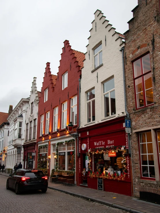 a car driving down a street next to tall buildings, a photo, by Jan Tengnagel, pexels contest winner, renaissance, small cottage with red shutters, local bar, flanders, humid evening