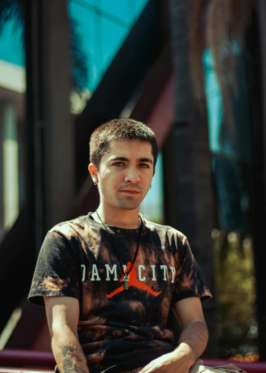 a man sitting on a bench in front of a building, an album cover, reddit, portrait of danny gonzalez, he is wearing a black t-shirt, 15081959 21121991 01012000 4k, hasbulla magomedov