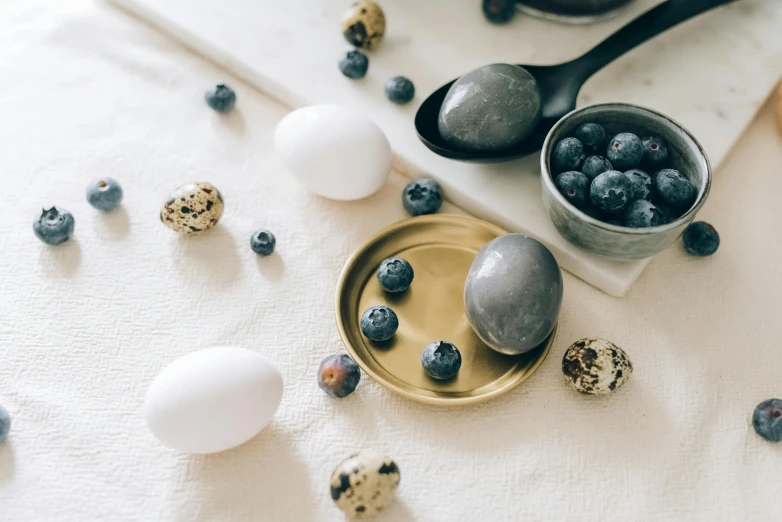 a white table topped with eggs and blueberries, a still life, by Emma Andijewska, trending on unsplash, miscellaneous objects, background image, shiny and metallic, miniature product photo