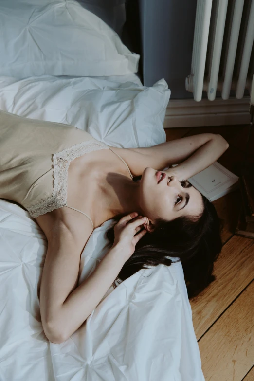 a woman laying on top of a bed next to a radiator, inspired by Elsa Bleda, trending on pexels, renaissance, soft pale golden skin, wearing white silk, brunette woman, lulu chen