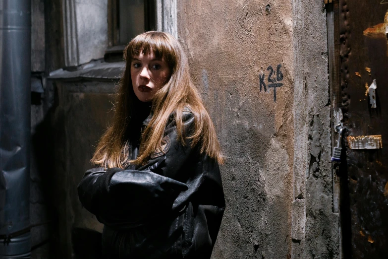 a woman in a black jacket leaning against a wall, inspired by Nan Goldin, pexels contest winner, graffiti, long hair with bangs, russian cinema, miranda otto as eowyn, bank robbery movies