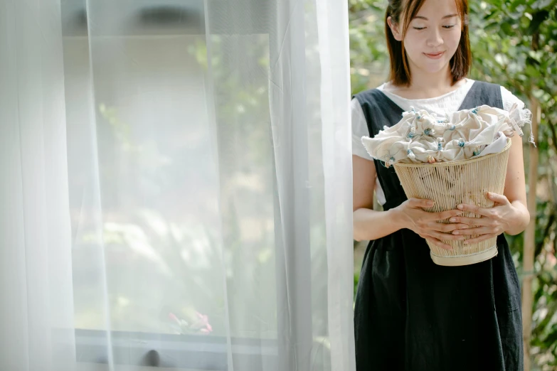 a woman in a black dress holding a basket of flowers, inspired by Kim Du-ryang, pexels contest winner, looking in the window, ( waitress ) girl, lined in cotton, ethereal curtain