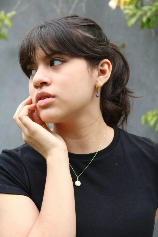 a woman in a black shirt talking on a cell phone, black and blue and gold jewelry, looking off to the side, round-cropped, pale-skinned persian girl