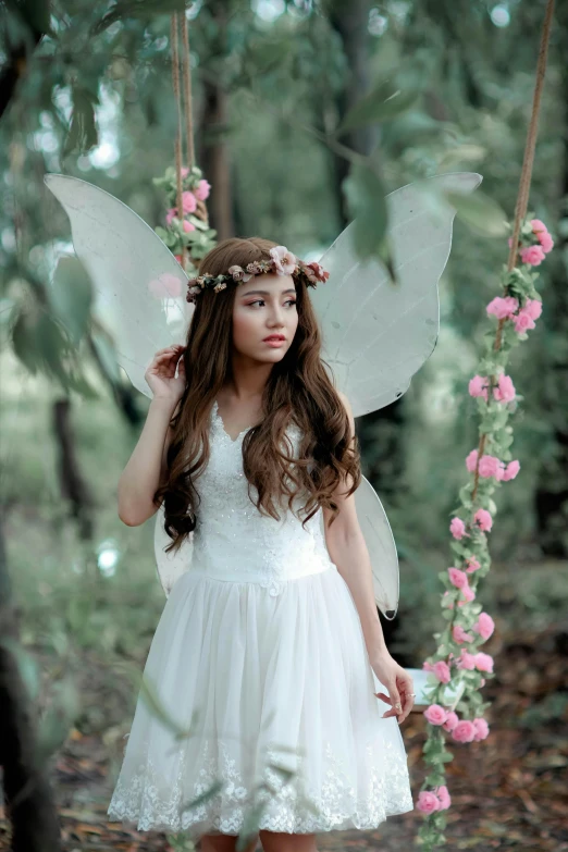 a woman in a white dress is sitting on a swing, by Marie Angel, pexels contest winner, renaissance, brunette elf with fairy wings, ulzzang, rose crown, butterfly