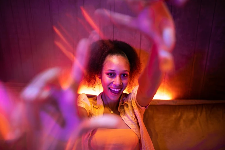 a woman sitting on a couch holding a remote control, interactive art, nightclub dancing inspired, wave a hand at the camera, warm coloured, dancing around a fire