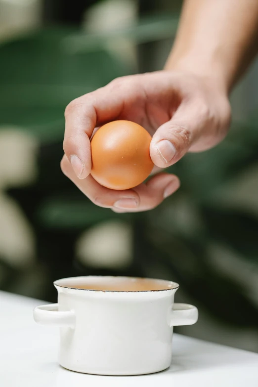 a person holding an egg over a cup of coffee, on a table, forshortening, ultra setting, an egg