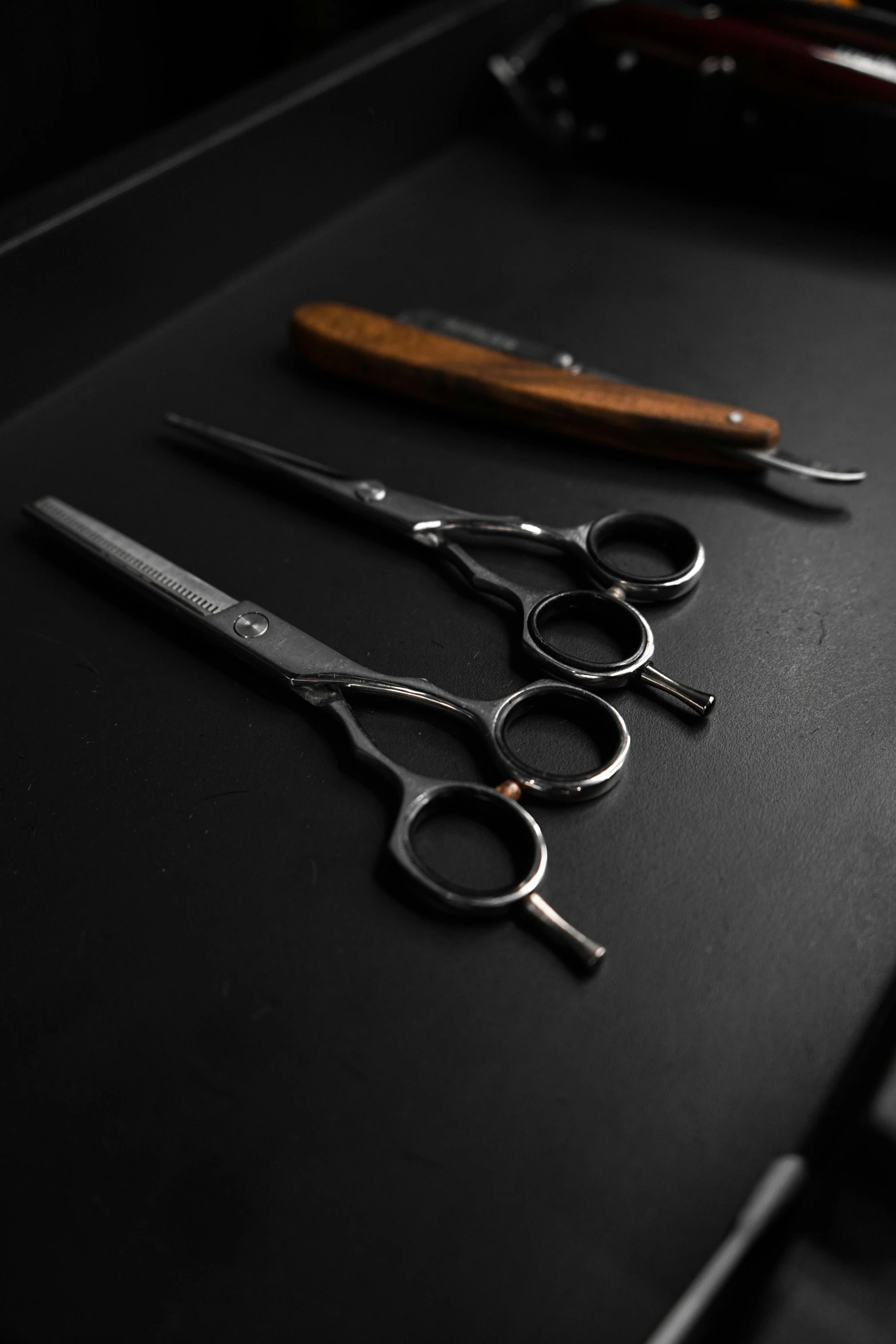 a pair of scissors sitting on top of a table, by Ben Zoeller, trending on pexels, hyperrealism, dark hairs, brown, technical, black and silver