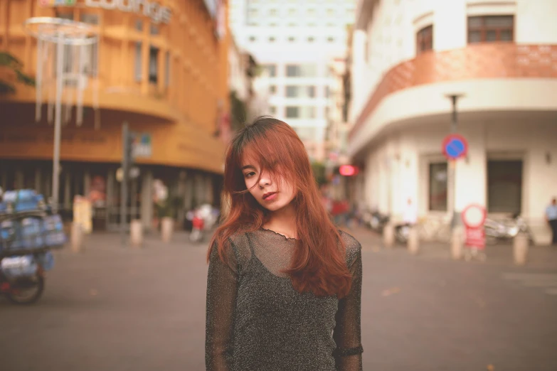 a woman standing in the middle of a street, by Tan Ting-pho, pexels contest winner, realism, brown-red-hair pretty face, 🤤 girl portrait, faded color, with glasses