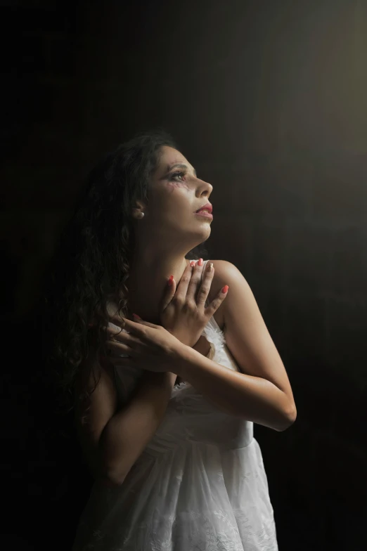 a woman in a white dress standing in front of a window, an album cover, inspired by Elsa Bleda, pexels contest winner, renaissance, praying posture, candid!! dark background, young woman looking up, provocative indian