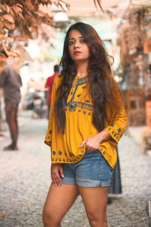 a woman standing in the middle of a street, by Riza Abbasi, pexels contest winner, wearing yellow floral blouse, dressed in a top and shorts, embroidered shirt, square