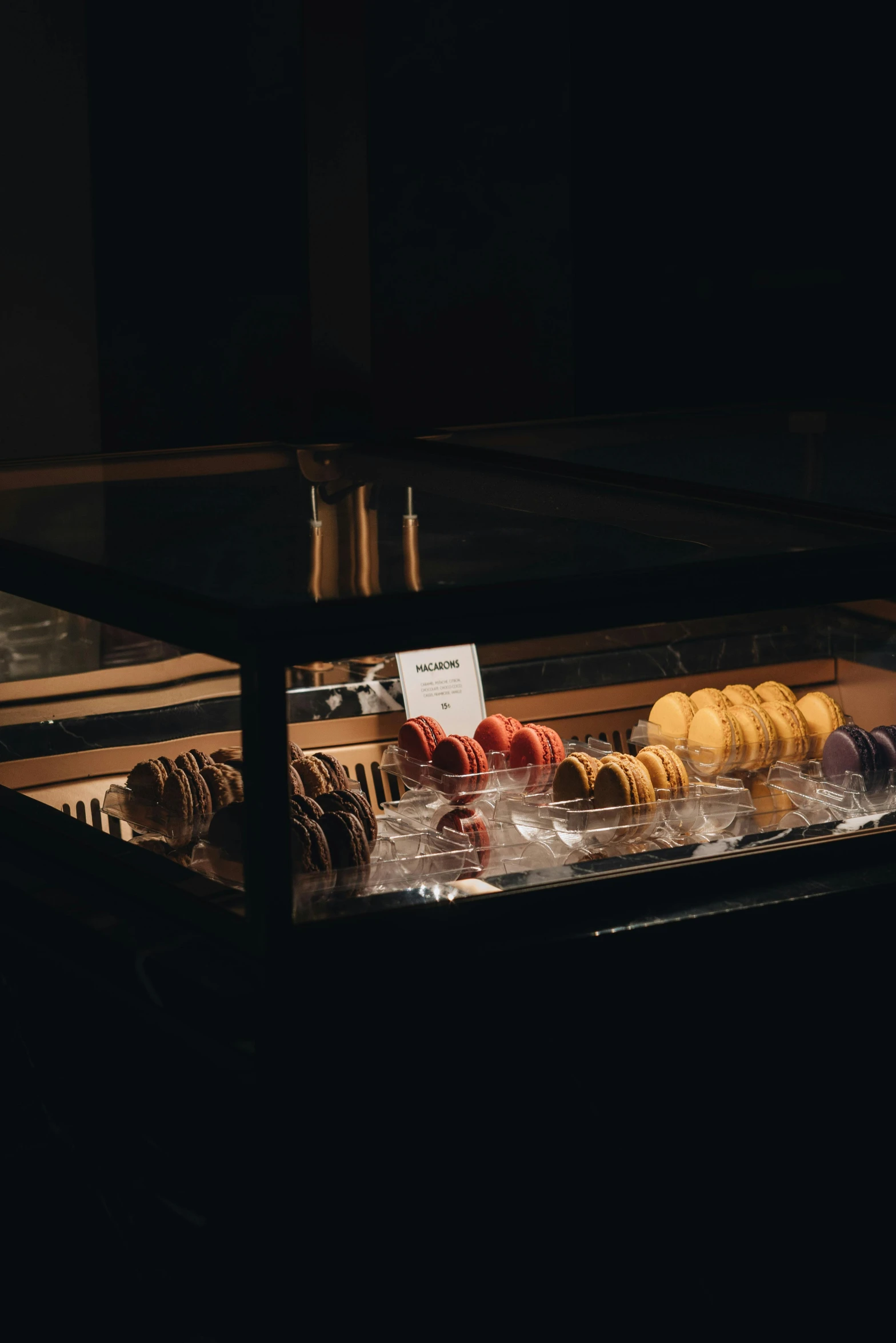 a display case filled with different types of donuts, a still life, inspired by Elsa Bleda, unsplash, very dark ambiance, macaron, sundown, nighthawks