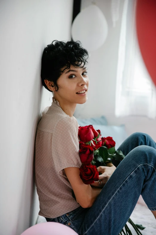 a woman sitting on a bed holding a bunch of roses, pexels contest winner, curly pixie cut hair, sarah andersen, wearing a shirt and a jean, maxim sukharev