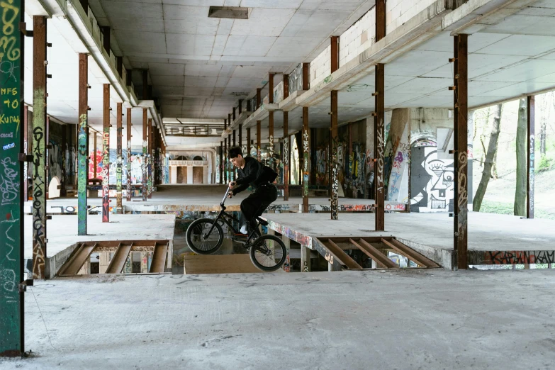 a man riding a bike up the side of a ramp, unsplash, graffiti, an abandonded courtyard, inside building, flattened, ignant