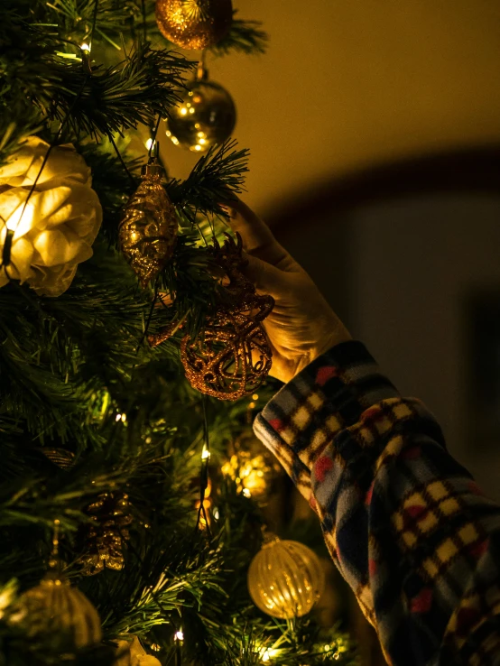 a person decorating a christmas tree with gold ornaments, by Julia Pishtar, happening, detailed ambient lighting, profile image, multiple stories, close angle