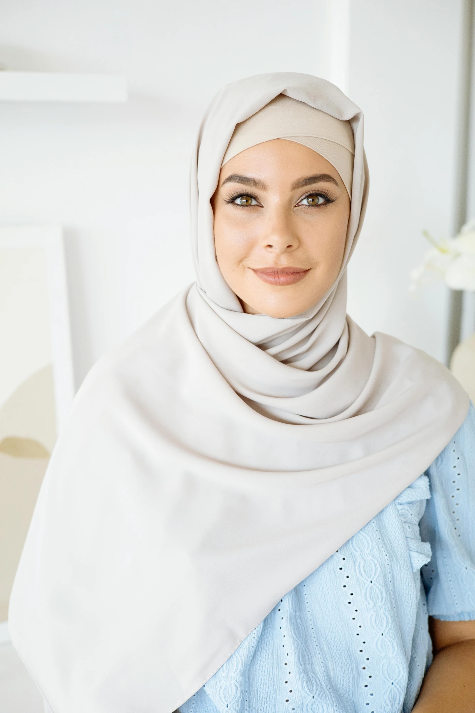 a woman sitting on a couch wearing a hijab, a picture, silver，ivory, smooth in _ the background, square face, milk and mocha style