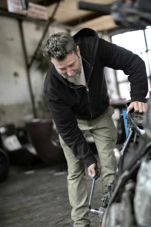 a man working on a motorcycle in a garage, grey, thumbnail, average, head down