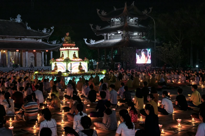 a group of people sitting on the ground with candles in front of them, guanyin, giant video screens, hoang lap, 8 k -