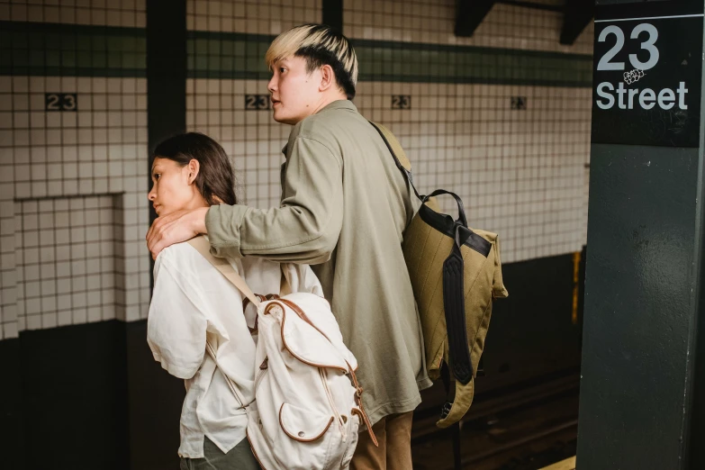 a couple of people standing next to each other on a train platform, by Nina Hamnett, trending on unsplash, happening, square backpack, green and brown clothes, asian man, wearing a linen shirt