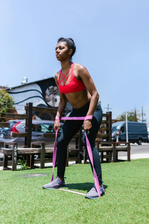 a woman standing on top of a lush green field, local gym, pink body harness, outside on the ground, photo of a black woman