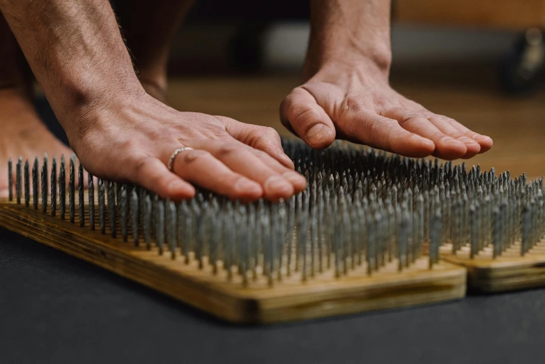 a close up of a person with nails on a board, by Jennifer Bartlett, unsplash, kinetic art, fibres trial on the floor, shodan, enormous hands, spiky