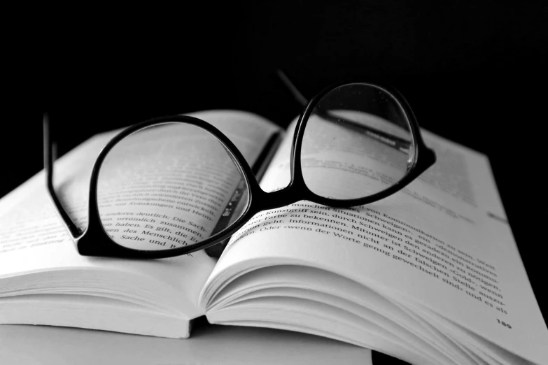 a pair of glasses sitting on top of an open book, a black and white photo, by Caroline Mytinger, pixabay, academic art, square rimmed glasses, open books, round black glasses, featured