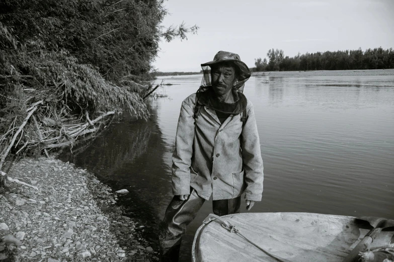 a black and white photo of a man standing next to a boat, pexels contest winner, process art, indigenous man, how river, photo courtesy museum of art, high drama