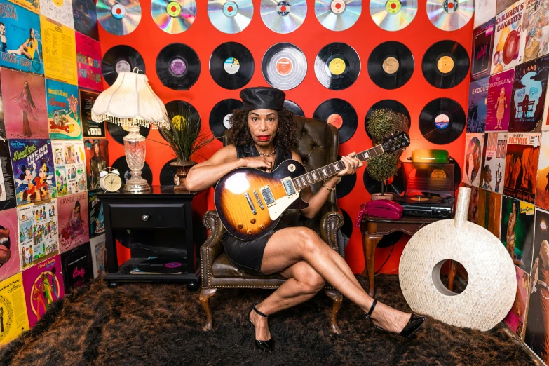 a woman sitting in a chair playing a guitar, an album cover, by Jeka Kemp, pexels, funk art, sitting on vintage leather sofa, bootsy collins, 15081959 21121991 01012000 4k, ashteroth