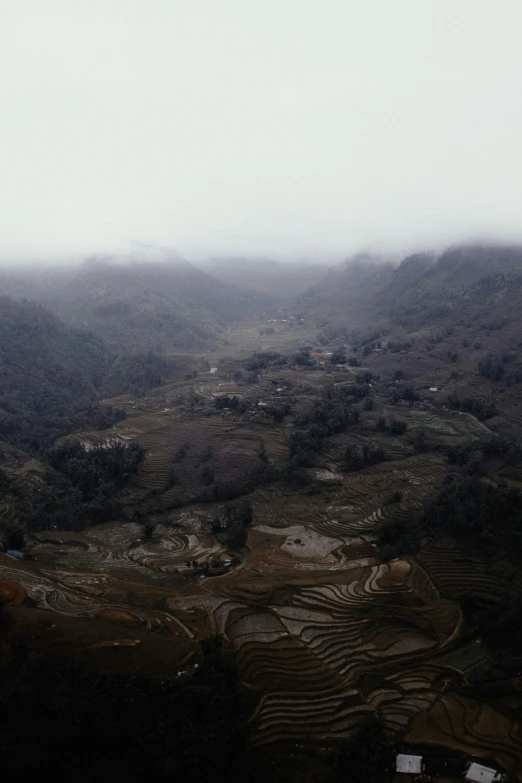 a view of a valley on a foggy day, hurufiyya, rice paddies, grey sky, dark, a high angle shot