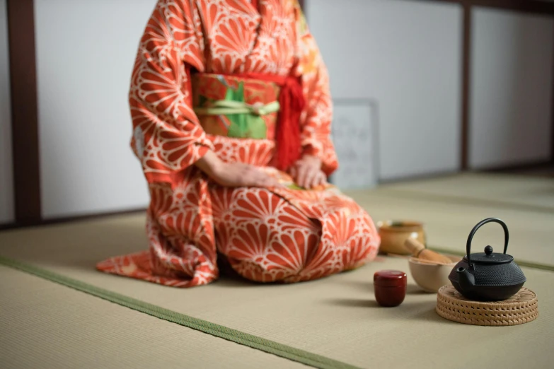 a woman in a kimono sitting on the floor, unsplash, is ((drinking a cup of tea)), red and gold cloth, けもの, in the center midground