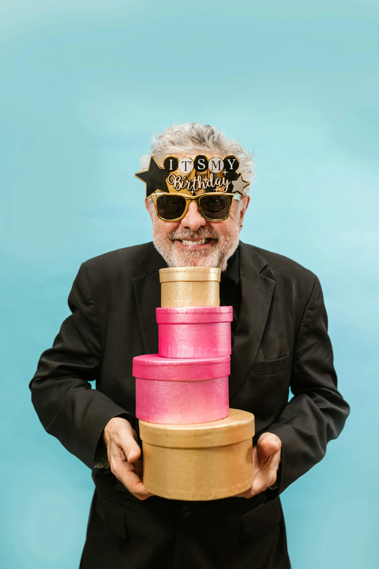 a man in a suit and sunglasses holding a cake, grey beard, birthday wrapped presents, sam nassour, press shot