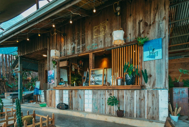 the outside of a restaurant with wooden tables and chairs, a portrait, unsplash, process art, beach bar, of augean stables, aussie baristas, ecovillage