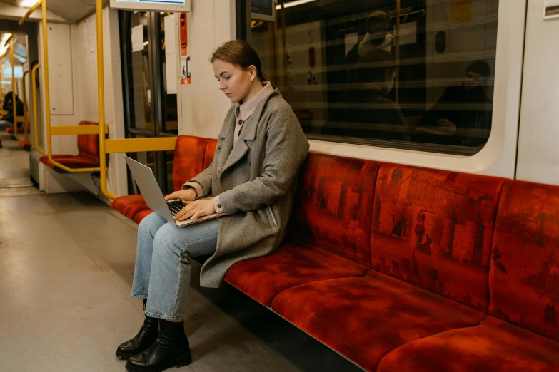 a woman sitting on a train with a laptop, by Emma Andijewska, pexels contest winner, happening, velvet couch, avatar image, underground, full length shot