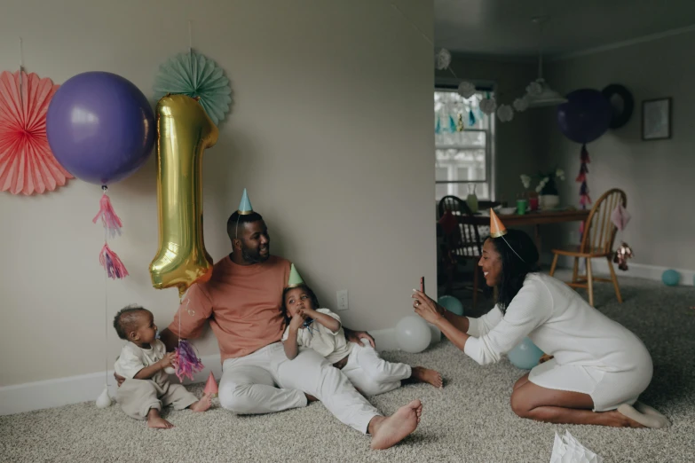 a group of people that are sitting on the floor, balloons, in a living room, fatherly, profile image