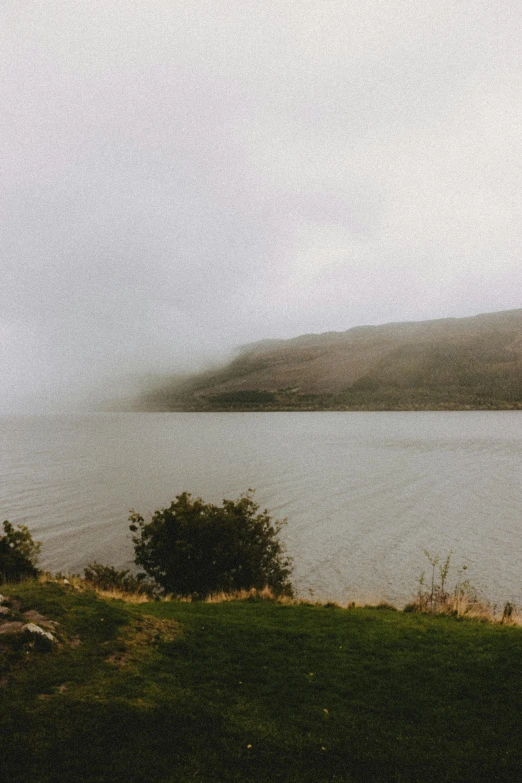 a large body of water sitting on top of a lush green hillside, a picture, unsplash, hudson river school, eerie and moody polaroid, gray fog, low quality photo, loch ness monster