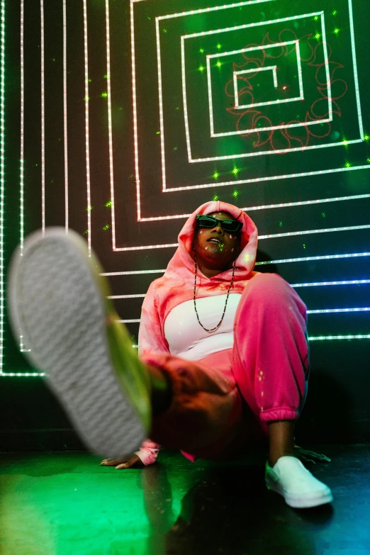 a man sitting on the ground in front of a neon wall, an album cover, unsplash, funk art, wearing a pink hoodie, performing on stage, woman with rose tinted glasses, focus on sneakers only