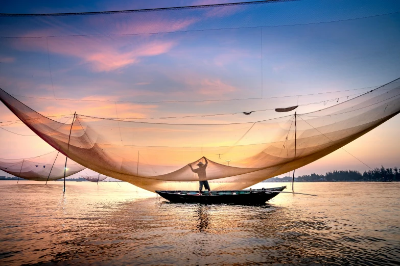 a man standing on top of a boat in the water, inspired by Steve McCurry, pexels contest winner, netting, in style of lam manh, warm glow, lined in cotton