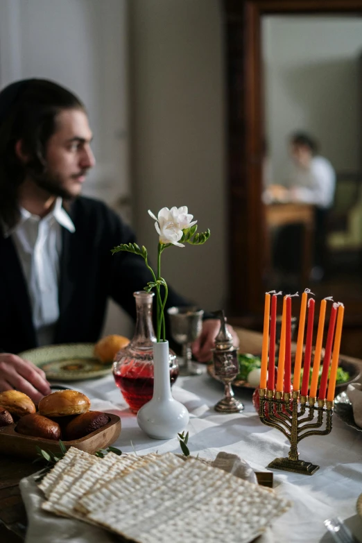 a man sitting at a table with a bunch of food, on a candle holder, hebrew, holiday season, moody iconic scene