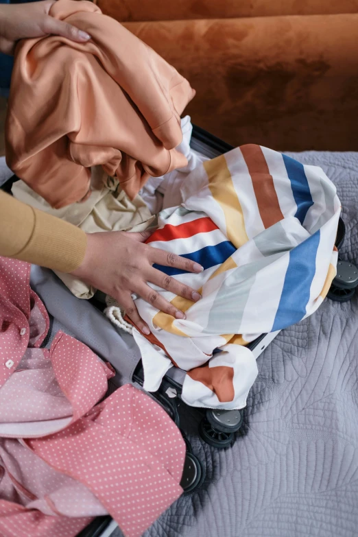 a person putting clothes in a suitcase on a bed, multicoloured, curated collections, centered shot, plastic and fabric