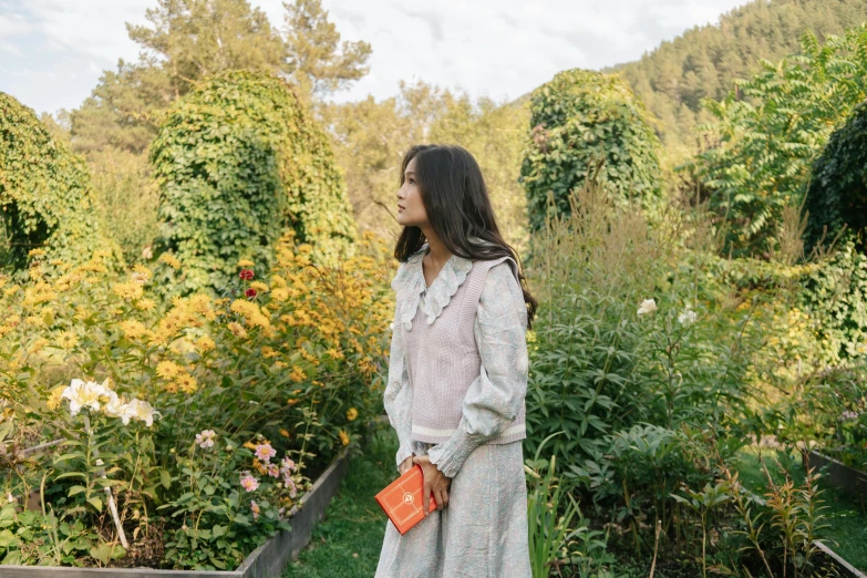 a woman standing in a garden holding an orange purse, unsplash, renaissance, song hye - kyo, in a cottagecore flower garden, in a valley, jackie tsai style